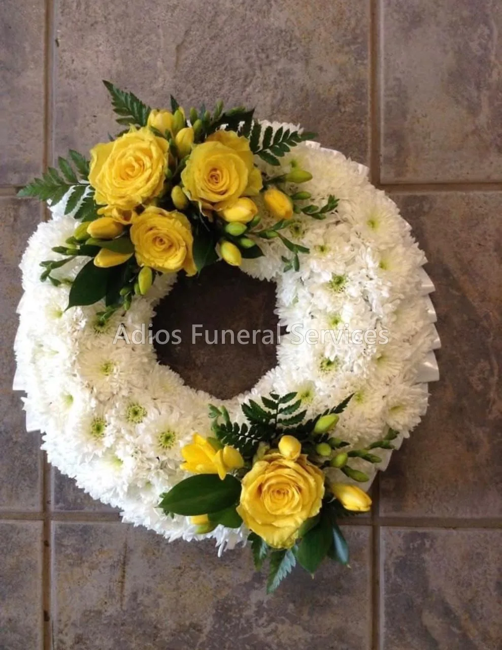 Circular funeral wreath of white chrysanthemums with yellow roses